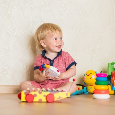 Toddler sitting on the floor surrounded by colorful toys.