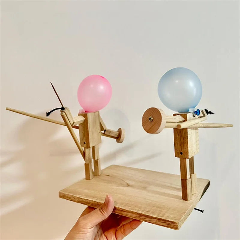 Woman's hand holding a wooden toy featuring two knight figures with balloons as heads with a goal of one popping the other. 