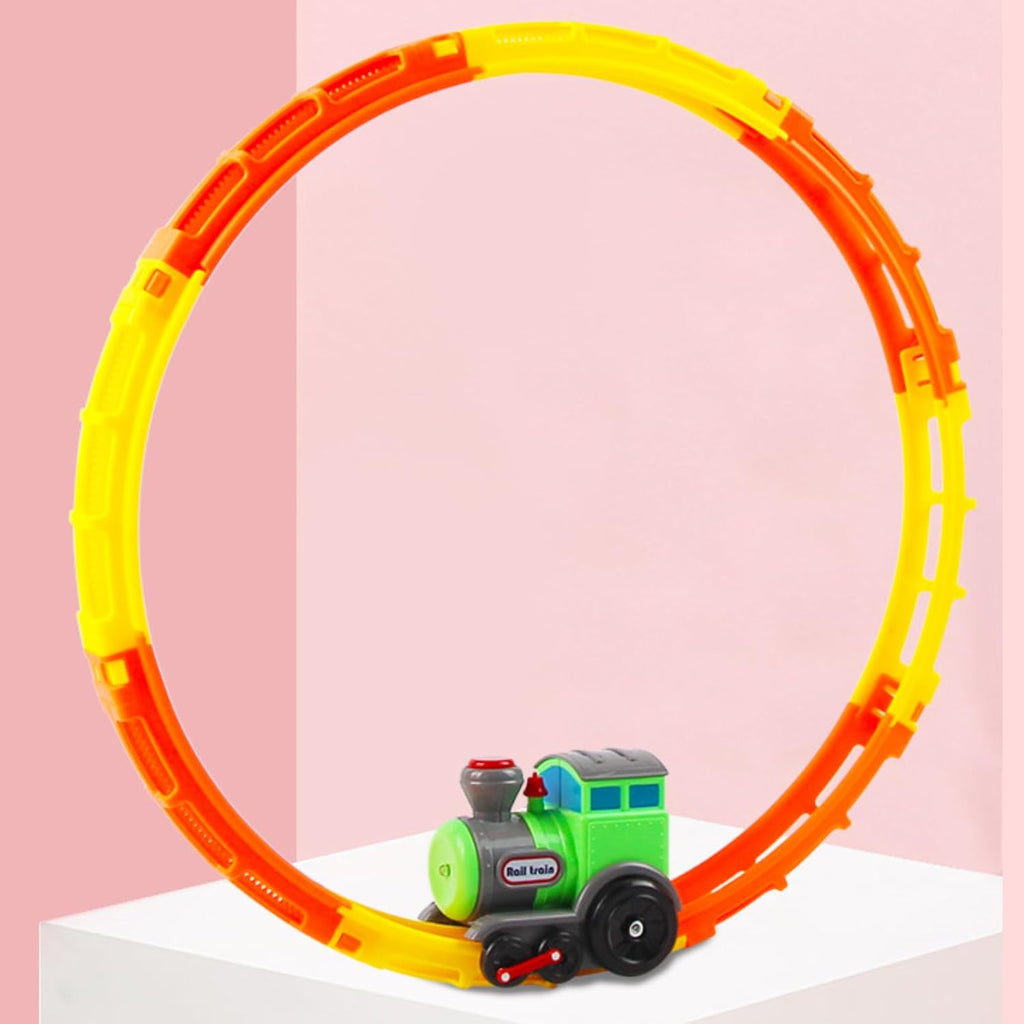 A green toy train on a circular yellow and orange loop track, placed on a white surface against a pink background. The track forms a complete vertical loop, demonstrating the train's movement capabilities.