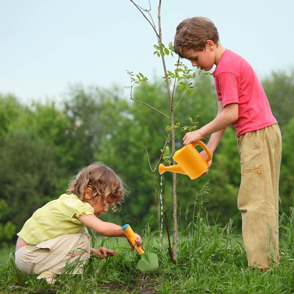Brother and sister watering a freshly planted tree using equipment from their Little Botanist Kit. 