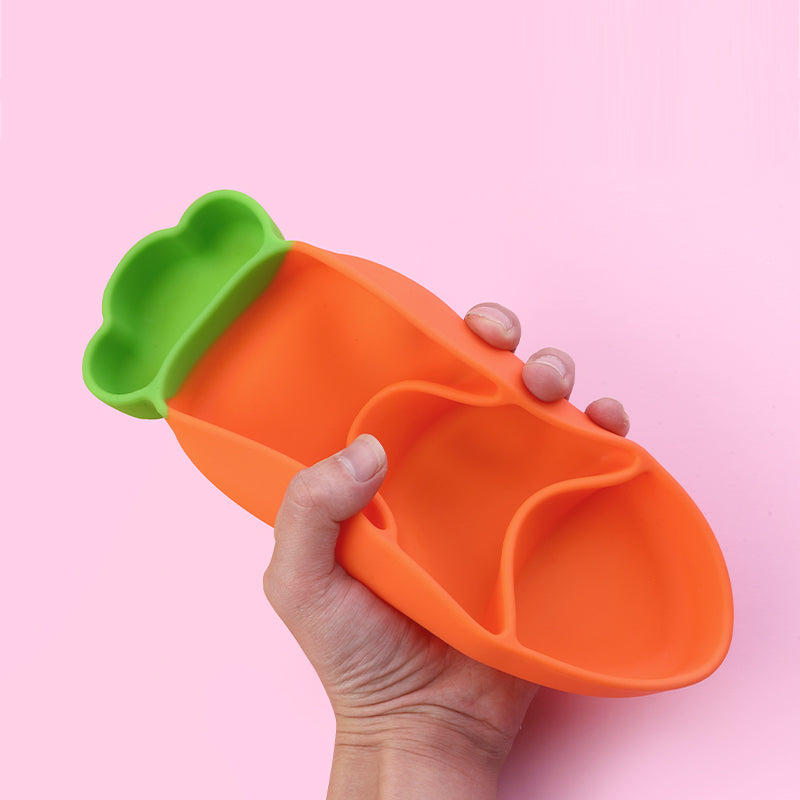 Hand holding a soft but durable carrot-shaped silicone plate, part of "My First Dining Set". 