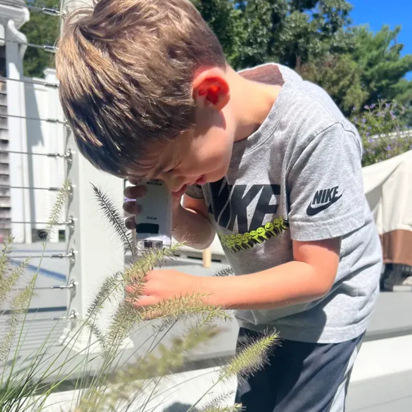 Preschooler boy exploring a herb outside his house with his Pocket Microscope by zooming on it.