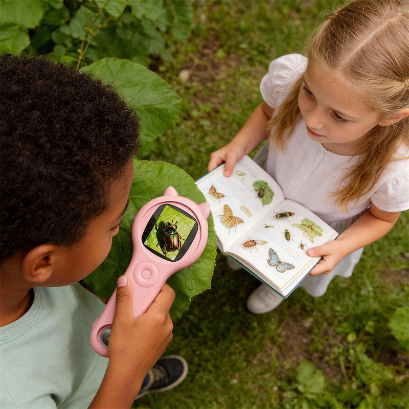 Two children exploring insects outdoors using a pink Little Scientist Microscope and an illustrated bug identification book for interactive science learning.